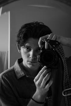 Grayscale Photo of a Man Holding Black DSLR Camera